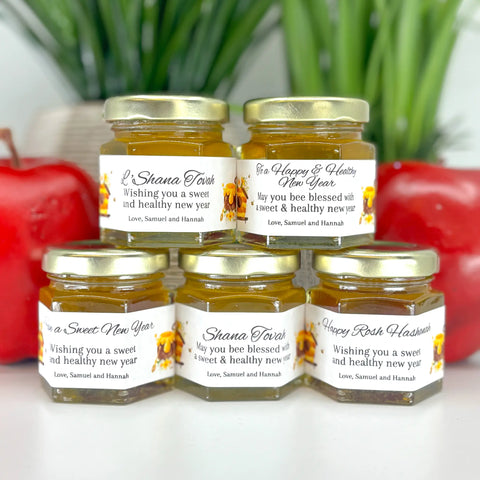 Close up of 2 oz honey Rosh Hashanah New Year favors on hexagon jars with gold lid with personalized honey-themed labels. Label titles shown are Have a Sweet New Year, Shana Tovah, Happy Rosh Hashanah, L'Shana Tovah, and To a Happy & Healthy New Year.