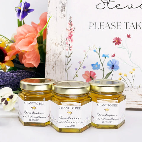 Close up of honey wedding favors with personalized meadow labels, 2 oz hexagon jars, and gold lids. Title on labels is Meant to Bee.